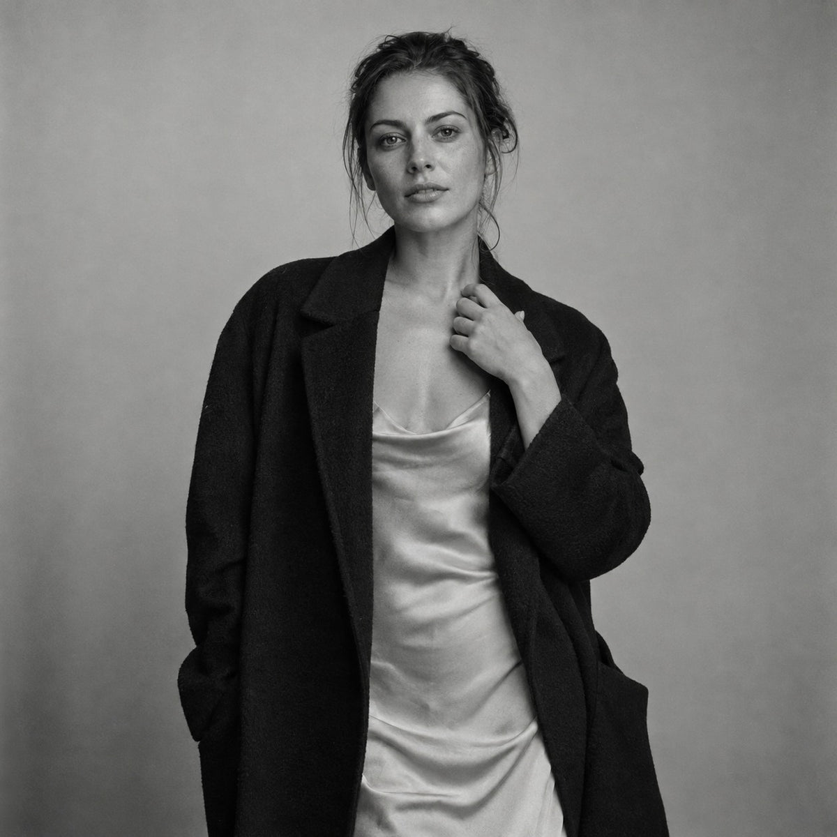 Woman in an oversized black coat over a silk slip dress, black and white studio portrait